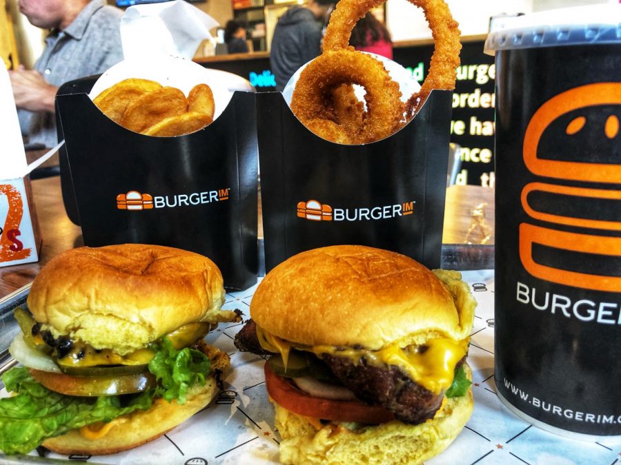 A classic beef and crispy chicken duo with a side of onion rings and signature Burgerim fries and a fountain drink sits fresh out of the kitchen.