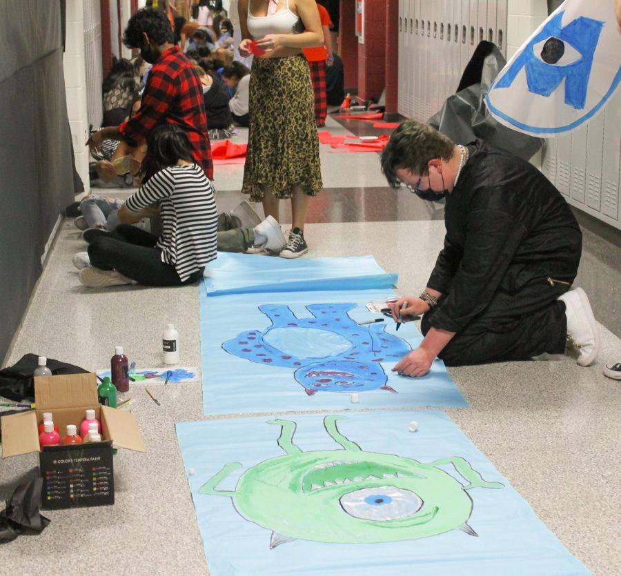 Kneeling over the blue construction paper, junior Danny Fortuno puts finishing touches on his painting of  Sully from Monsters Inc.