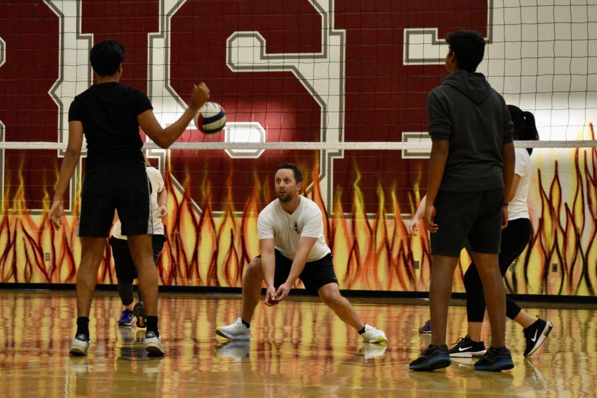 English teacher Tyler Anderson positions himself in the path of the ball, aiming to bump it back over the net to the students.