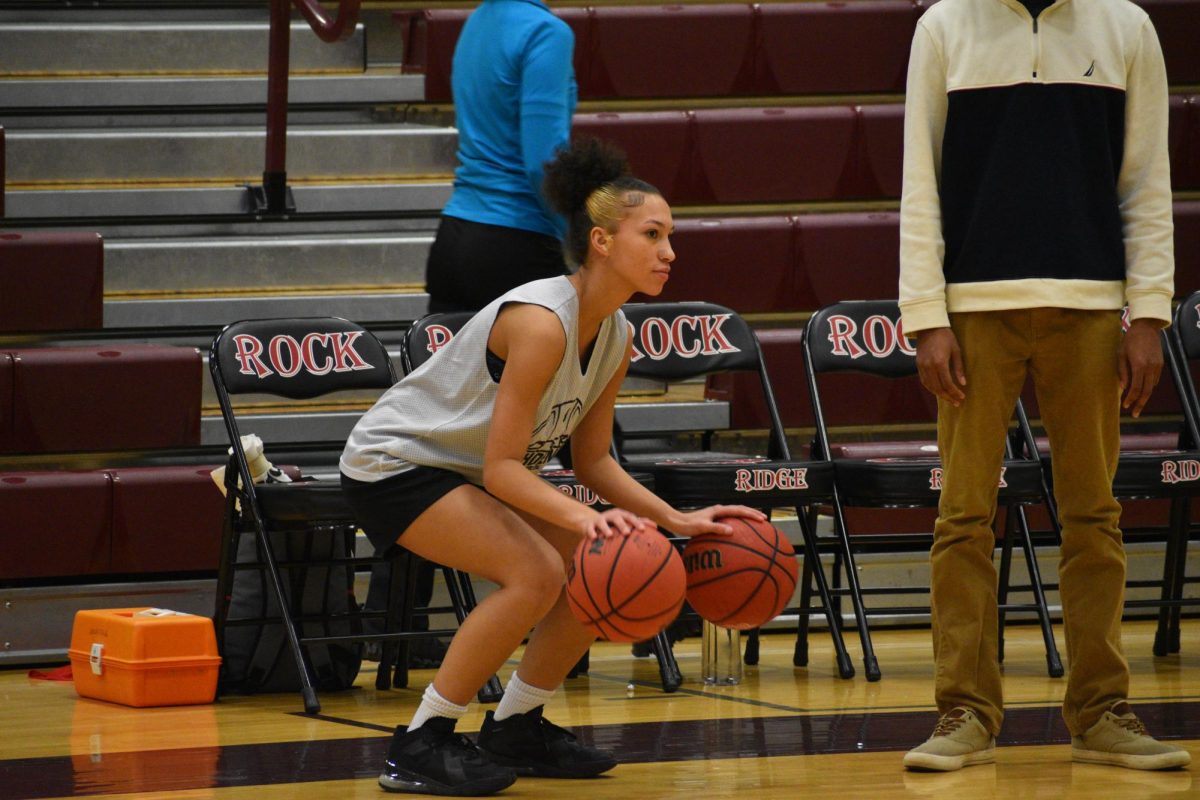 Before the game starts, senior Cora Bowen dribbles two basketballs while sitting on the bench.