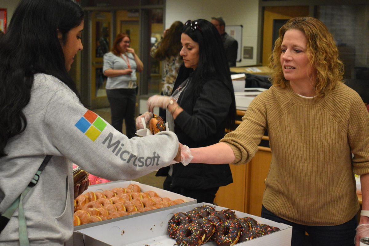 Parent volunteer Ami Adams hands a senior a chocolate-covered donut as she enters the breakfast.