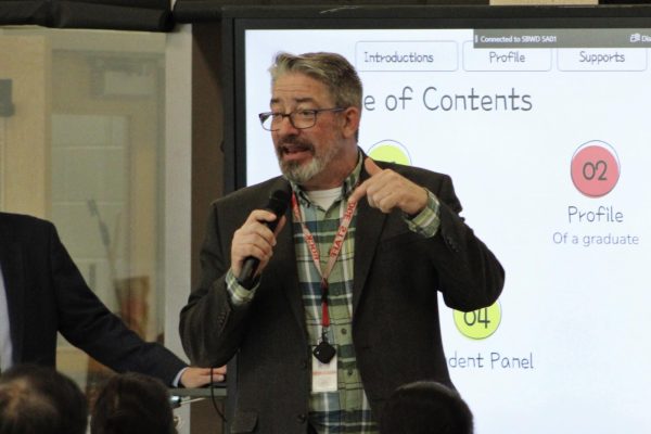 Speaking into the microphone, Principal John Duellman speaks to the parents of rising fifth-grade and eighth-grade students.