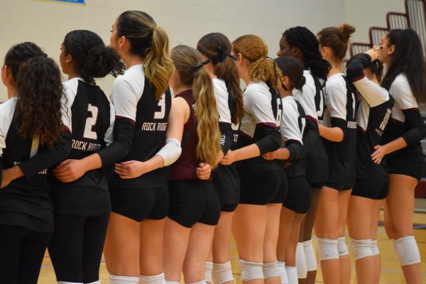 The Phoenix varsity volleyball team lines up for the national anthem. “We were more communicative [with each other] during this game, and I feel like we kept our energy up, especially after the first set,” senior Jessica Valdov said. 