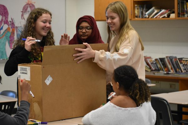 Members of the Cure Club, including president Mimtaaha Kader (center) and member Sadie Cluck (right), work on a donation box for a fundraising event during a meeting. 