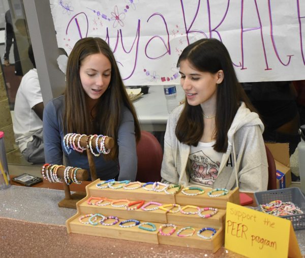 PEER members juniors Maya Waas and Olivia Wilkins sit at a table, selling bracelets for a fundraiser.