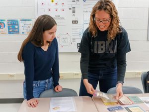 AP world history and US history teacher Megan Adair and sophomore Alexandra Takach talk to each other while analyzing pieces of propaganda replicas from WWII. “I think it’s really interesting to put what they’ve learned in the classroom and then visualize it,” Takach said. “Across all aspects, culturally and then also messages and gas masks, and pamphlets, just to see what they are talking about in effect.”