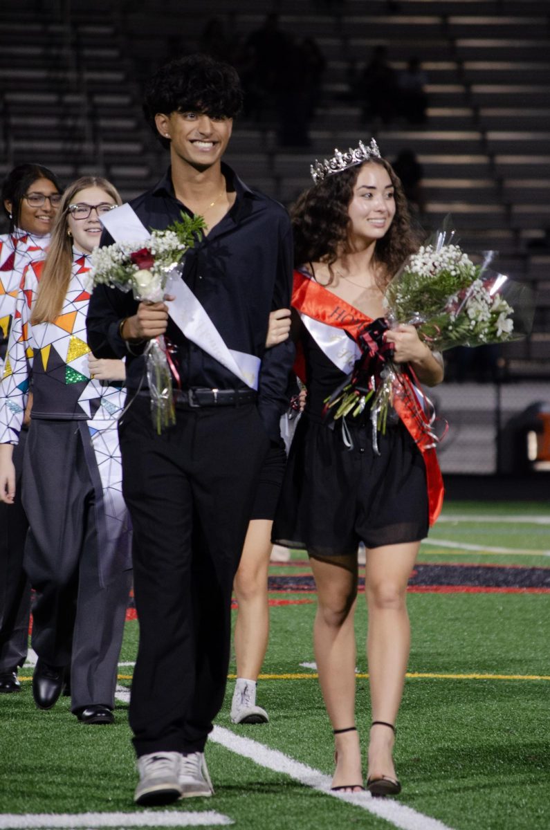 Seniors Kenidy Nguyen and Arya Lele walk down the field with cheers from the crowd, after Nguyen was crowned homecoming royalty.